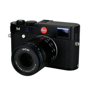 Laowa_85mm_f_5_6_2X_Ultra_Macro_APO_002 Musta Leica M -kamera, johon on kiinnitetty Laowa 85mm f/5.6 2X Ultra-Macro APO - Sony FE -objektiivi, kuvattuna kameran ja objektiivin etu- ja sivupuolelta valkoista taustaa vasten.