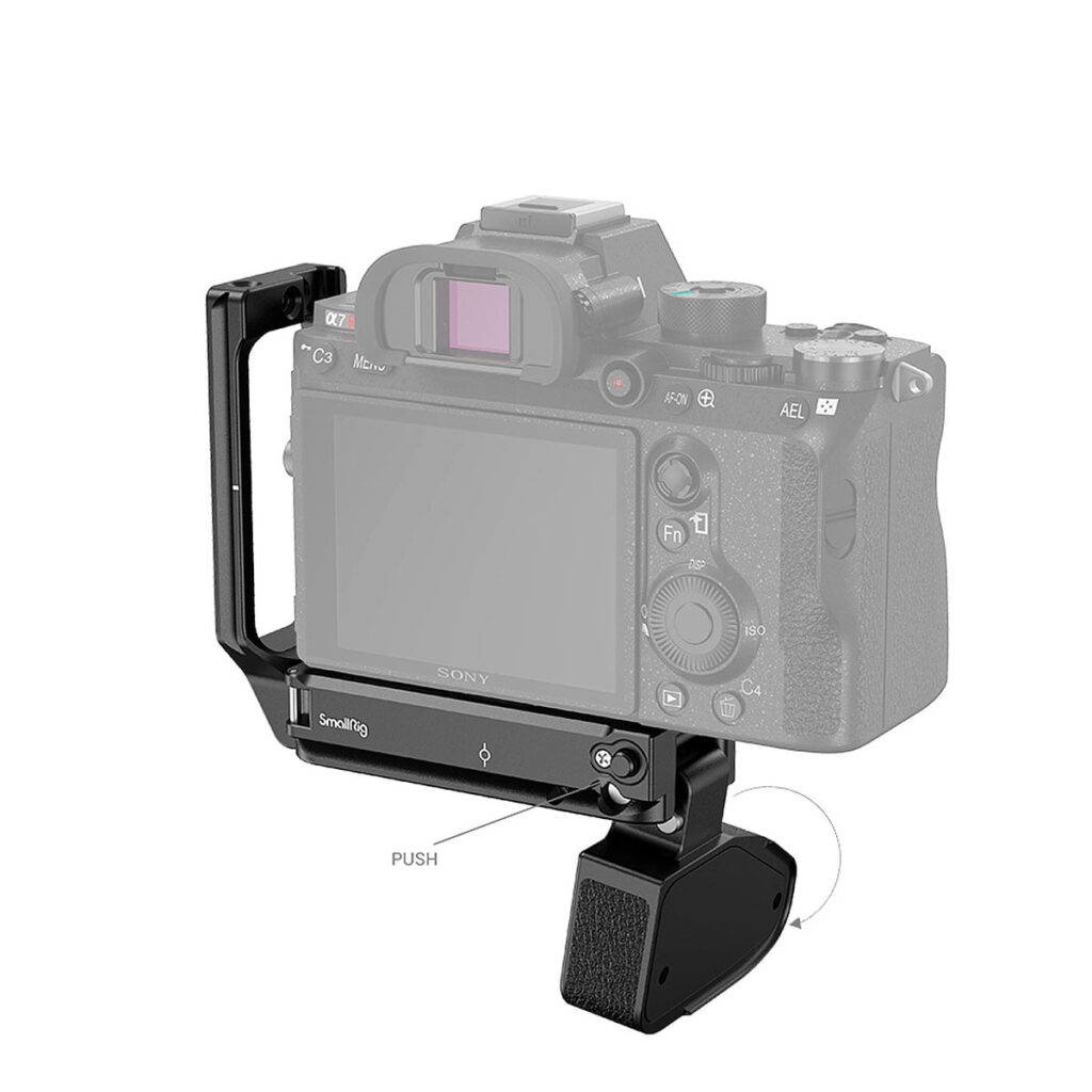 SmallRig_2417_L-Bracket_for_Sony_Alpha_7R_IV_Alpha_9_II_LCS_005 SmallRig 2417 L-kiinnike Sony Alpha 7R IV:lle ja Alpha 9 II:lle on kuvassa kiinnitettynä kameraan, ja siinä on kuvioitu kahva ja painike helppoa irrottamista varten. Kameran runko näkyy osittain harmaana kiinnikkeen korostamiseksi.