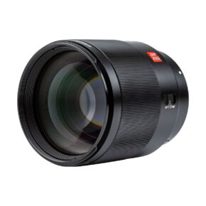 Lähikuvassa Viltrox AF 85mm f/1.8 AF II - Canon RF -objektiivista näkyy sen musta, kuvioitu tynnyri, suuri etulasielementti ja automaattitarkennuksen/manuaalitarkennuksen kytkin valkoista taustaa vasten.
