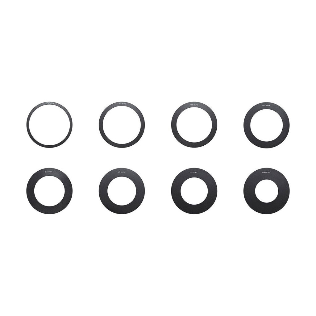 Godox_MF12_Set_of_Adapter_Rings_001 Kahdeksan mustaa pyöreää metallirengasta Godox MF12 -sovitinrenkaista on sijoitettu kahteen riviin valkoiselle taustalle, ja jokaisessa on pieni valkoinen teksti.