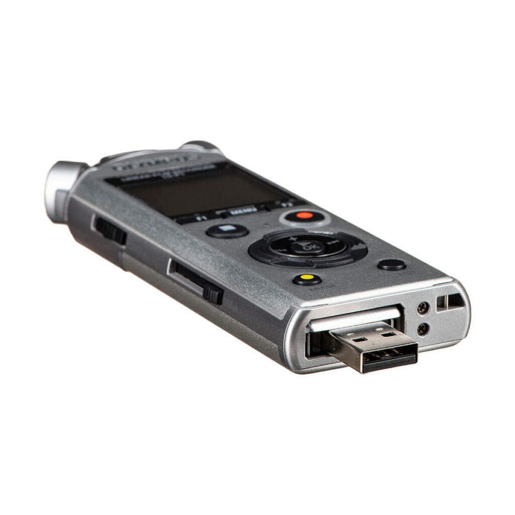Olympus_LS-P1_0008 Olympus LS-P1 -äänitallentimessa on sisäänrakennettu USB-liitin, musta näyttö, useita ohjauspainikkeita ja hopeanvärinen metallirunko valkoisella pohjalla.