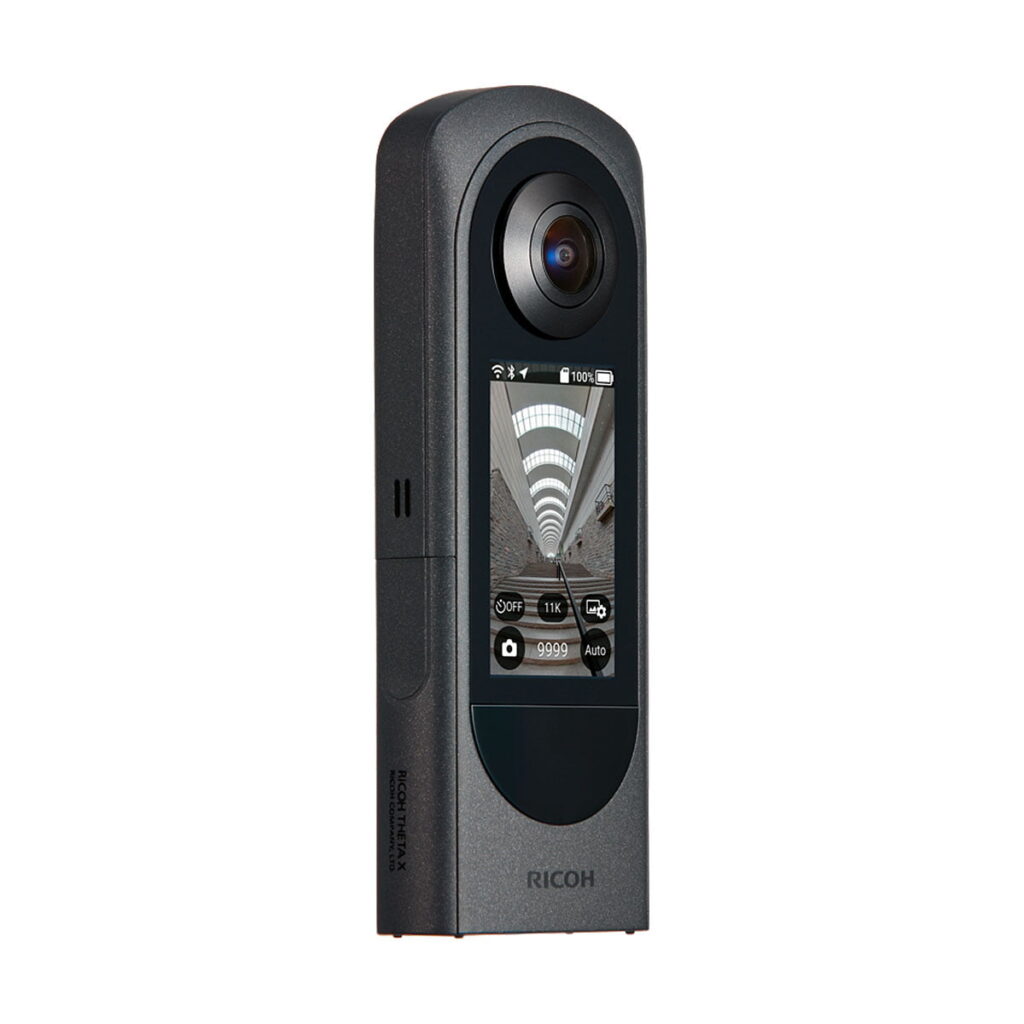 Ricoh_Theta_X_006 Mustassa Ricoh Theta X 360 asteen kamerassa, jossa on värinäyttö, näkyy live-käytävän esikatselu. Kamera seisoo pystyasennossa, ja siinä näkyy objektiivi, painikkeet ja Ricohin tuotemerkki.