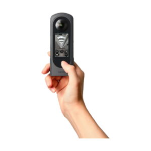 Ricoh_Theta_X_007 Kädessä on Ricoh Theta X, musta 360 asteen kamera, jonka pienellä näytöllä on kalansilmäkuva ja ohjauskuvakkeita.