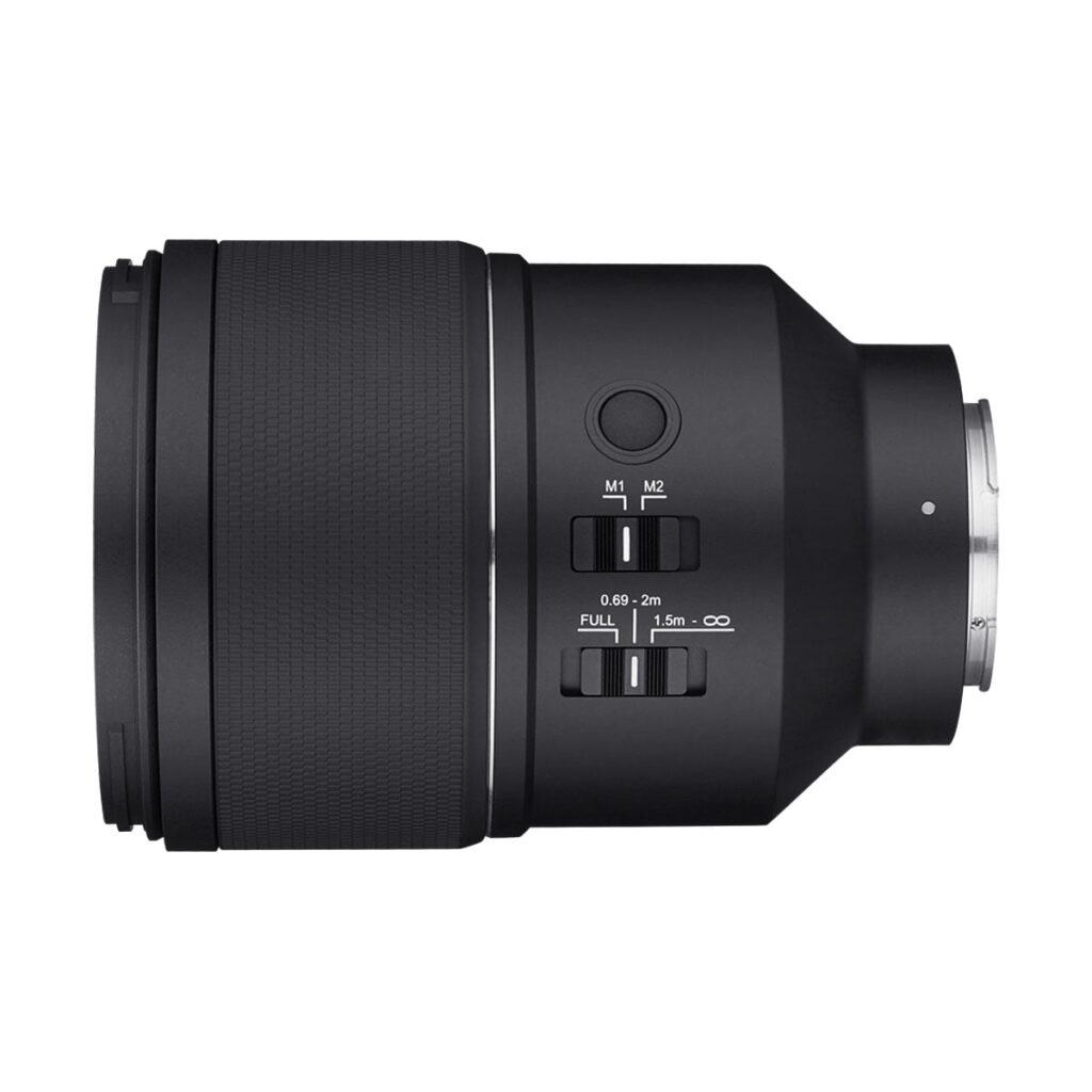 Samyang_AF_135mm_F_1_8_Sony-FE_003 Samyang AF 135mm F/1.8 - Sony FE -objektiivin sivukuva mustana, jossa on ohjauskytkimet, painikkeet, kuvioitu tarkennusrengas ja metallinen objektiivin kiinnike oikealla, valkoista taustaa vasten.