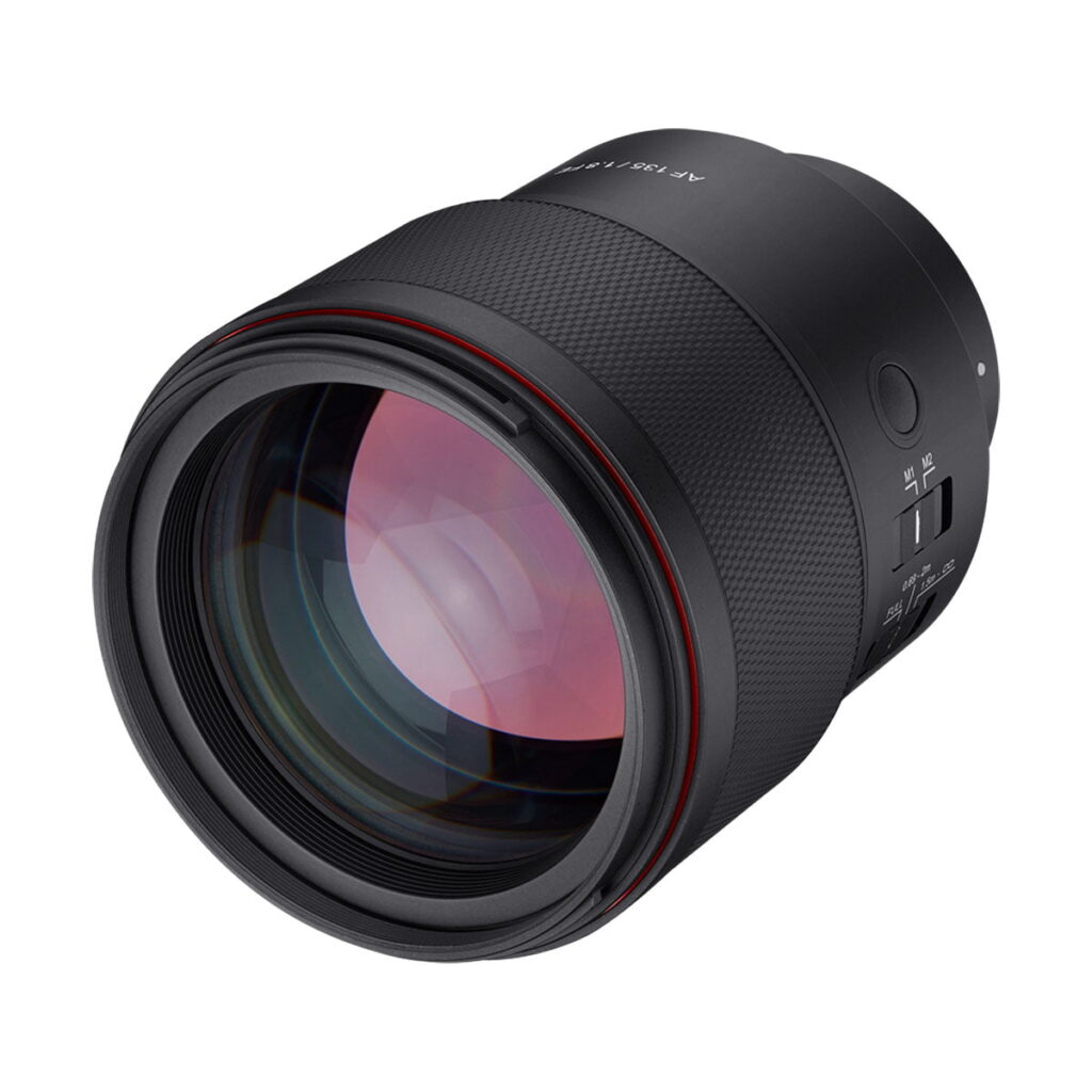 Samyang_AF_135mm_F_1_8_Sony-FE_005 Lähikuvassa Samyang AF 135mm F/1.8 - Sony FE -objektiivista näkyy sen musta kuvioitu kahva, kytkimet ja heijastavat lasielementit valkoista taustaa vasten.