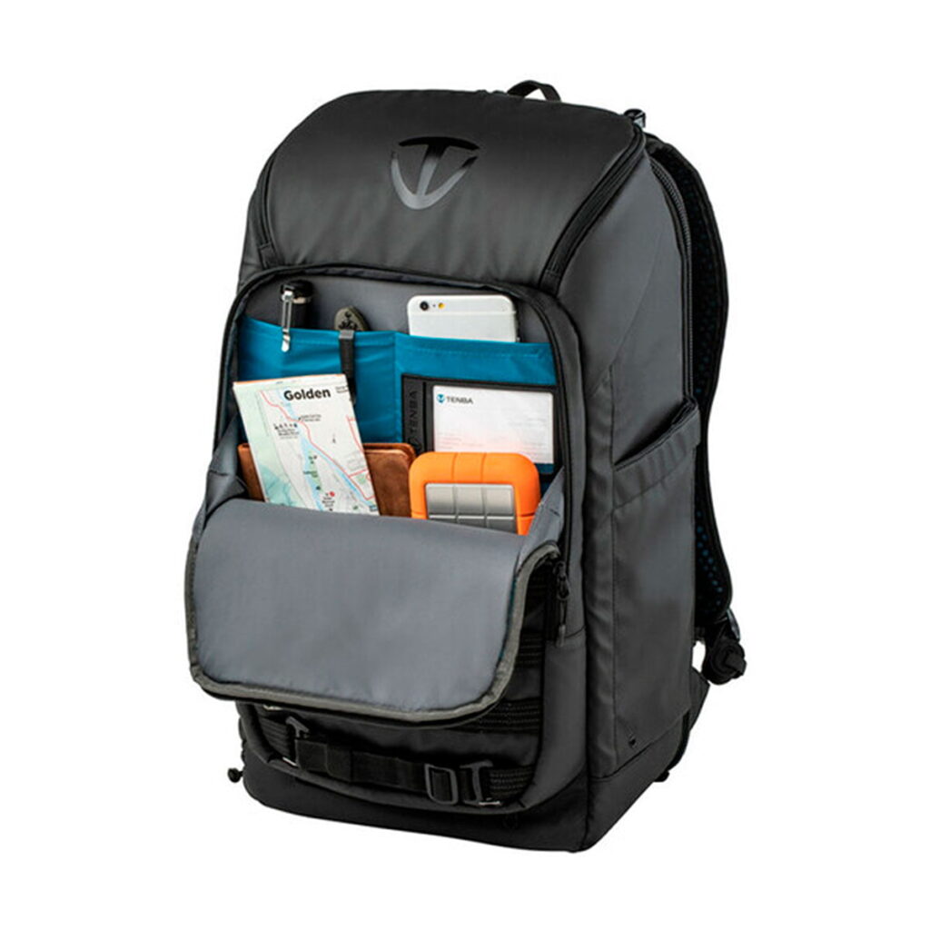 Tenba_Axis_20L_Tactical_Backpack_004 Mustassa Tenba Axis 20L Tactical Backpack -repussa on etutasku auki, ja siinä on kartta, muistikirja, puhelin, kyniä ja oranssi ulkoinen kiintolevy merkittyihin lokeroihin.