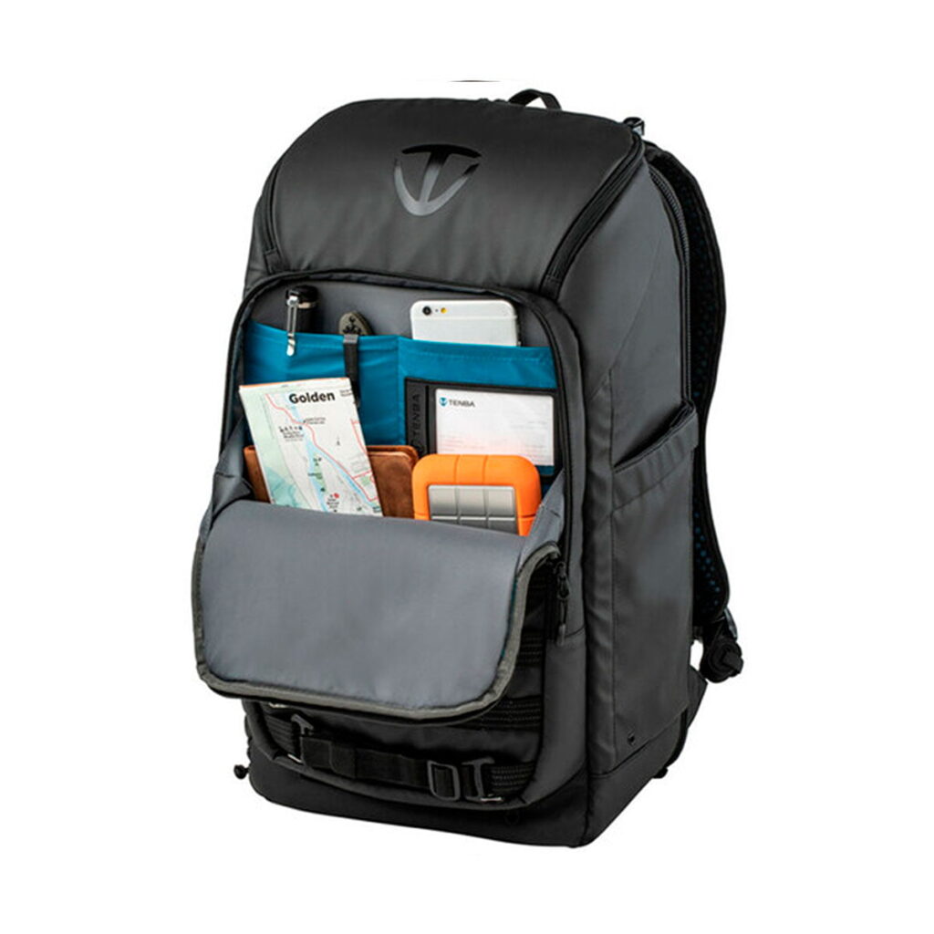 Tenba_Axis_24L_Tactical_Backpack_004 Tenba Axis 24L Tactical Backpack seisoo pystyasennossa valkoisella pohjalla, ja sen etutasku on avattu paljastaen järjestetyt lokerot, joihin mahtuu siististi kartta, puhelin, muistikirja, kyniä ja oranssi kiintolevy.