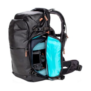 Shimoda Designs Explore v2 25 Starter Kit -kamerareppu, musta, sisältää pehmustetun sinisen sisustan, useita lokeroita kameravarusteiden järjestettyyn säilytykseen ja ruskeat vetoketjunvetimet. Osittain avattu vetoketju paljastaa kameran turvallisesti säilöttynä sisälle.