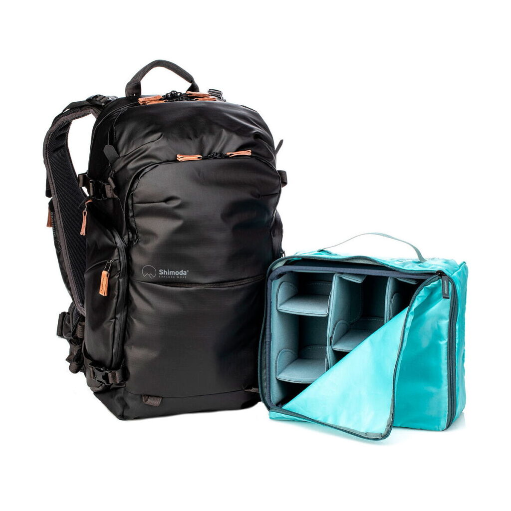 Shimoda Designs Explore v2 25 Starter Kit -kamerareppu, musta on esillä turkoosin värisen kameravarusteiden järjestäjän vieressä, jossa on pehmustetut lokerot ja avoin läppä.