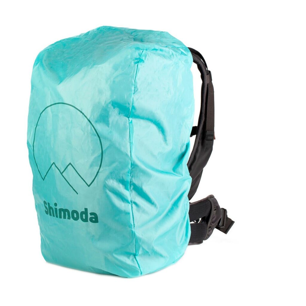 Mustan Shimoda Designs Explore v2 25 Starter Kit -kamerarepun, jossa on pehmustetut olkahihnat ja vyötäröhihna, päälle on asennettu turkoosi sadesuoja, jossa on "Shimoda" ja vuoristologo.