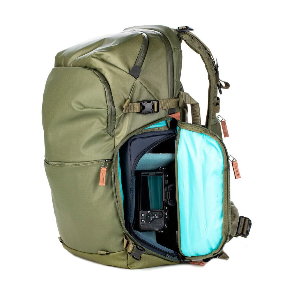 Shimoda Designs Explore v2 30 -kamerareppu, vihreä seisoo pystyssä sivutasku auki vetoketjulla, ja sen turkoosilla vuoratun pehmustetun lokeron sisällä on kamera.