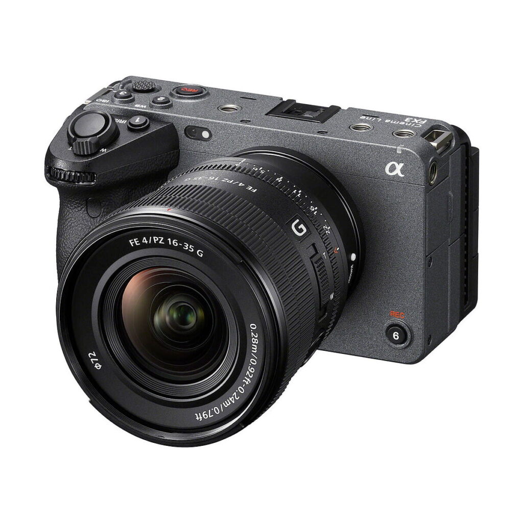 Sony_FE_PZ_16-35mm_f_4_G_008 Musta Sony-digitaalikamera, jossa on Sony FE PZ 16-35mm f/4 G -objektiivi ja useita painikkeita ja valitsimia, näkyy vinossa valkoisella taustalla.