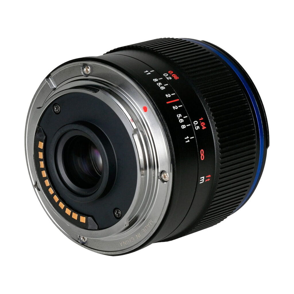Laowa_7_5mm_f_2_MFT_Auto_Aperture_Version_008 Lähikuva Laowa 7,5 mm f/2 MFT AE -objektiivista takaa, jossa korostuvat sen metallinen kiinnitysrengas, elektroniset koskettimet ja osa tarkennusrenkaasta, jossa on näkyvissä etäisyys- ja aukkomerkinnät.
