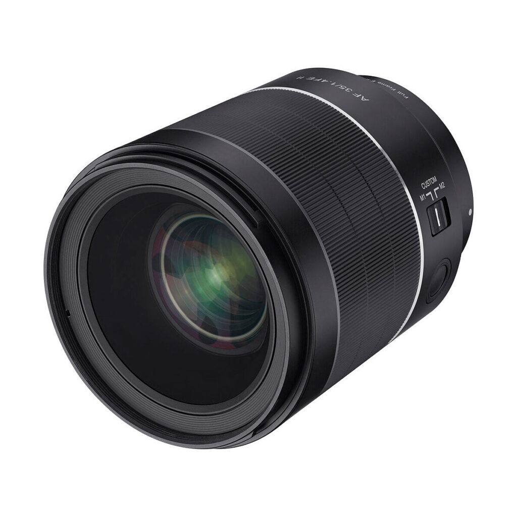 Samyang_35mm_f_1_4_AF_II_004 Lähikuvassa Samyang AF 35mm f/1.4 II - Sony E -objektiivista näkyy sen suuri lasielementti, säätörenkaat ja kytkimet AF/MF ja CUSTOM valkoista taustaa vasten kuvattuna.