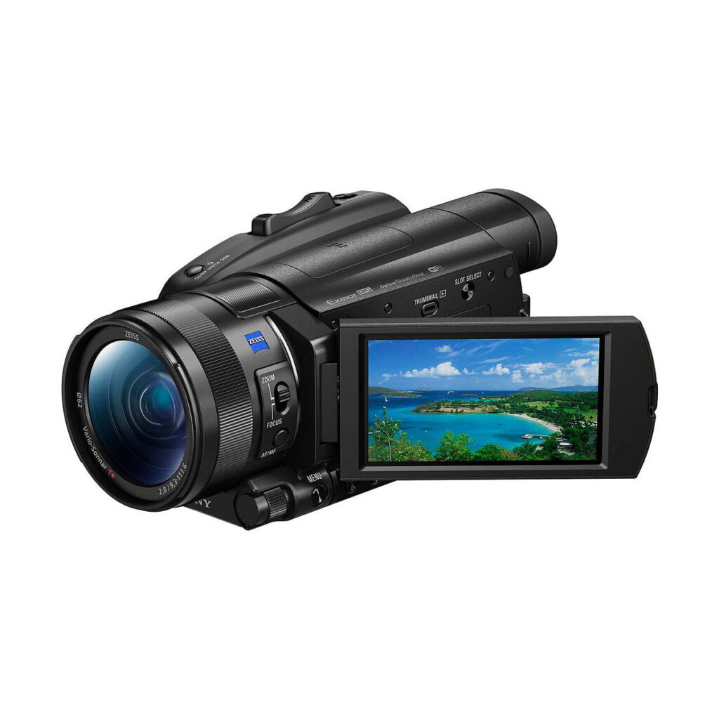 Sony_FDR-AX700_001 Sony FDR-AX700 4K -videokamerassa on musta muotoilu ja sivulle käännettävä LCD-näyttö, joka näyttää maiseman, jossa on sinistä vettä, vihreitä puita ja pilvinen taivas.