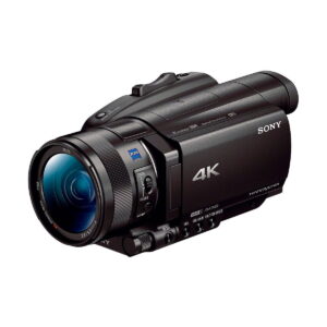 Sony_FDR-AX700_003 Musta Sony FDR-AX700 4K -videokamera, jossa on suuri objektiivi, useita ohjauspainikkeita ja käsikahva, näkyy etupuolelta valkoista taustaa vasten.