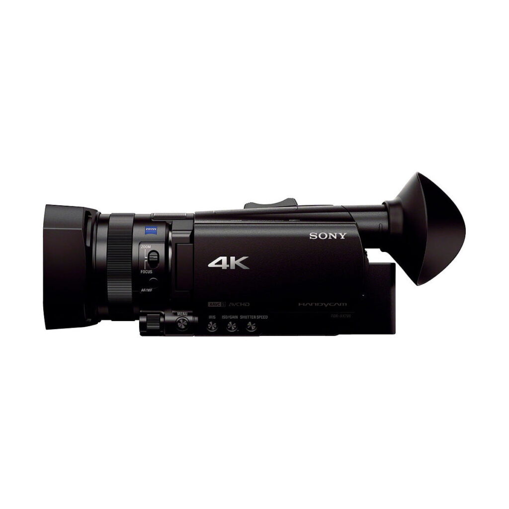 Sony_FDR-AX700_004 Mustan Sony FDR-AX700 4K -videokameran sivukuva, jossa on suuri objektiivi, ohjauspainikkeet ja näkyvä okulaari valkoista taustaa vasten.