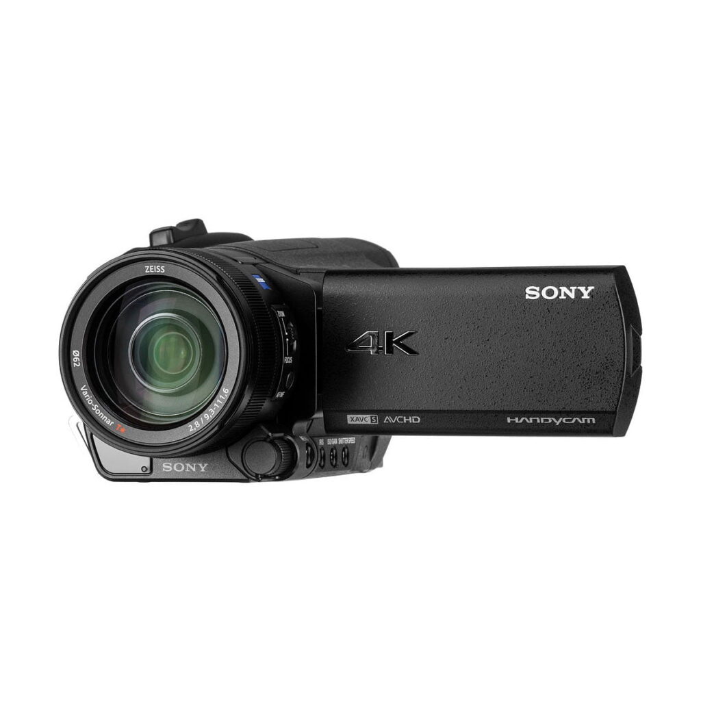 Sony_FDR-AX700_008 Kuvassa on musta Sony FDR-AX700 4K -videokamera, jossa on Zeiss-objektiivi, avoin LCD-näyttö ja useita sivupainikkeita.