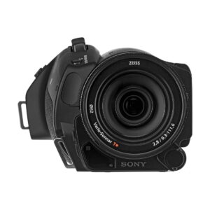 Sony_FDR-AX700_010 Sony FDR-AX700 4K -videokameran musta etukuva Zeiss Vario-Sonnar -objektiivilla, jossa näkyy objektiivin yksityiskohdat ja kuvioitu vasen kahva valkoista taustaa vasten.