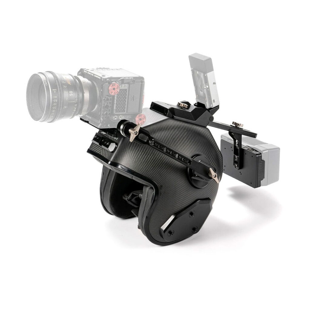 Tilta_Hermit_POV_Camera_Support_Helmet_V-Mount_005 Tilta Hermit POV-kameratukikypärä (M, V-Mount) on musta kypärä, johon on asennettu kameralaitteet - kamera, monitori ja akkupaketti - jotka on kiinnitetty metallisilla kannattimilla ja käsivarsilla. Jotkin osat on esitetty osittain läpinäkyvinä kypärän korostamiseksi.