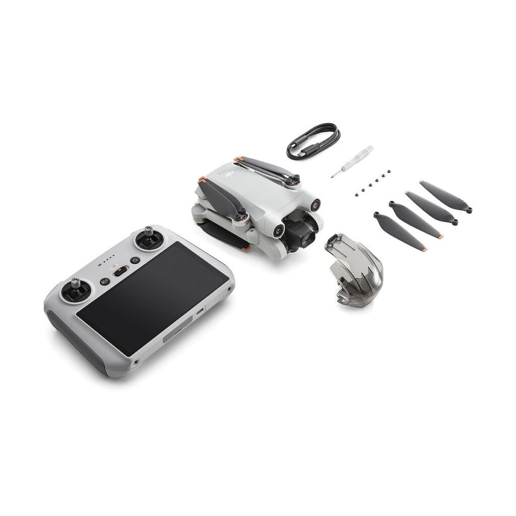 DJi_Mini_3_Pro_Smart_Controller_000 DJI Mini 3 Pro + Smart Controller -pakkaus sisältää kokoontaitetun lennokin, älykkään ohjaimen, akun, latauskaapelin, ruuvimeisselin, neljä potkuria ja neljä pientä ruuvia, jotka on järjestetty siististi valkoiselle taustalle.