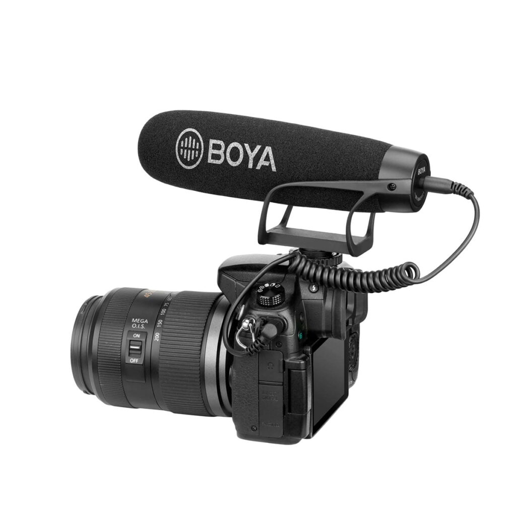 Boya-BY-BM2021-2 Zoom-objektiivilla varustetun digitaalikameran päälle on asennettu suuri Boya BY-BM2021 3,5 mm:n haulikko-kondensaattorimikrofoni, joka on yhdistetty kelattuun äänikaapeliin, eristettynä valkoiselle taustalle.