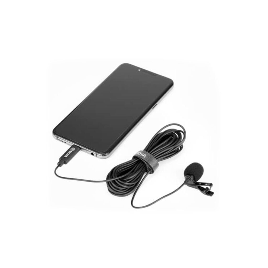 Boya-BY-M3-2 Boya BY-M3 Lavalier USB-C -mikrofoni, jossa on klipsi, on yhdistetty älypuhelimeen, ja molemmat on asetettu valkoiselle pinnalle. Mikrofonin kaapeli on osittain kierretty ja kiinnitetty tarranauhalla.