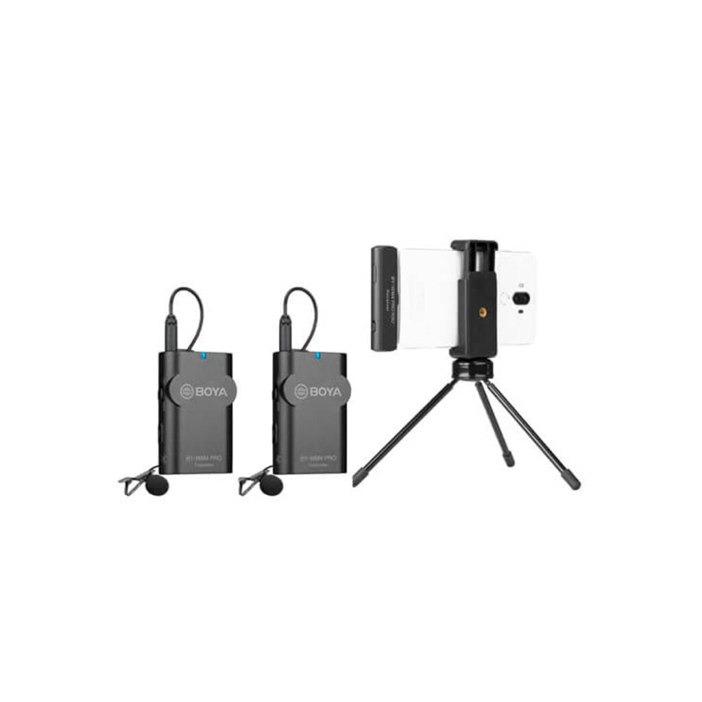 Kaksi BOYA BY-WM4 Pro K6 x2 Langaton USB-C mikrofonijärjestelmä-lähetintä, joissa on lavalier-mikrofoni, on esillä älypuhelimen vieressä mustalla jalustalla ja puhelimen pidikkeellä, kaikki valkoista taustaa vasten.