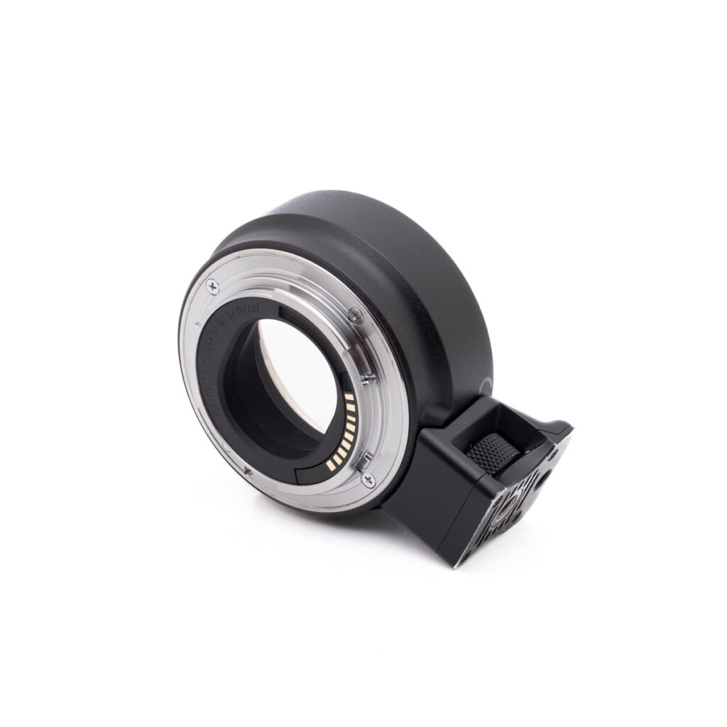 Canon EF-EOSM adapter-3 Lähikuva Canon EOS M50 - Käytetty -kameran objektiivisovittimesta, jossa on metallinen kiinnitysrengas, elektroniset koskettimet ja musta muovirunko valkoista taustaa vasten.
