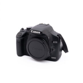 Canon Eos 500D-1 Käytetty Sigma 30mm f/1.4 DC DN -objektiivi Sony E -kiinnitykseen, kuvattuna kulmassa, objektiivin suojus päällä valkoista taustaa vasten.