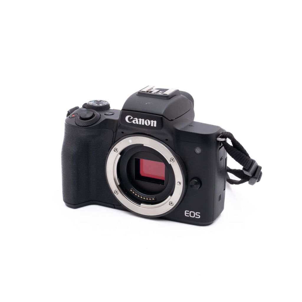 Canon M50-2 Musta Canon EOS M50 - Käytetty peilitön kamerarunko ilman objektiivia, jossa näkyy kenno ja objektiivin kiinnitys, sekä kiinnitetty käsihihna valkoisella taustalla.