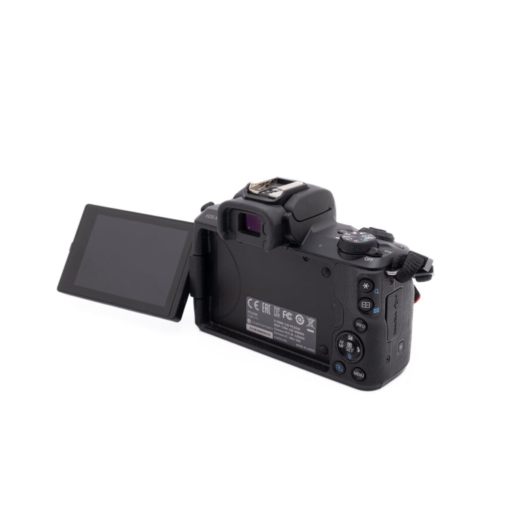 Canon M50-3 Canon EOS M50 - Käytetty mustan värinen digitaalikamera, jonka LCD-näyttö on käännetty vasemmalle, jolloin takaosan painikkeet ja säätimet näkyvät, kuvattuna valkoisella pohjalla.