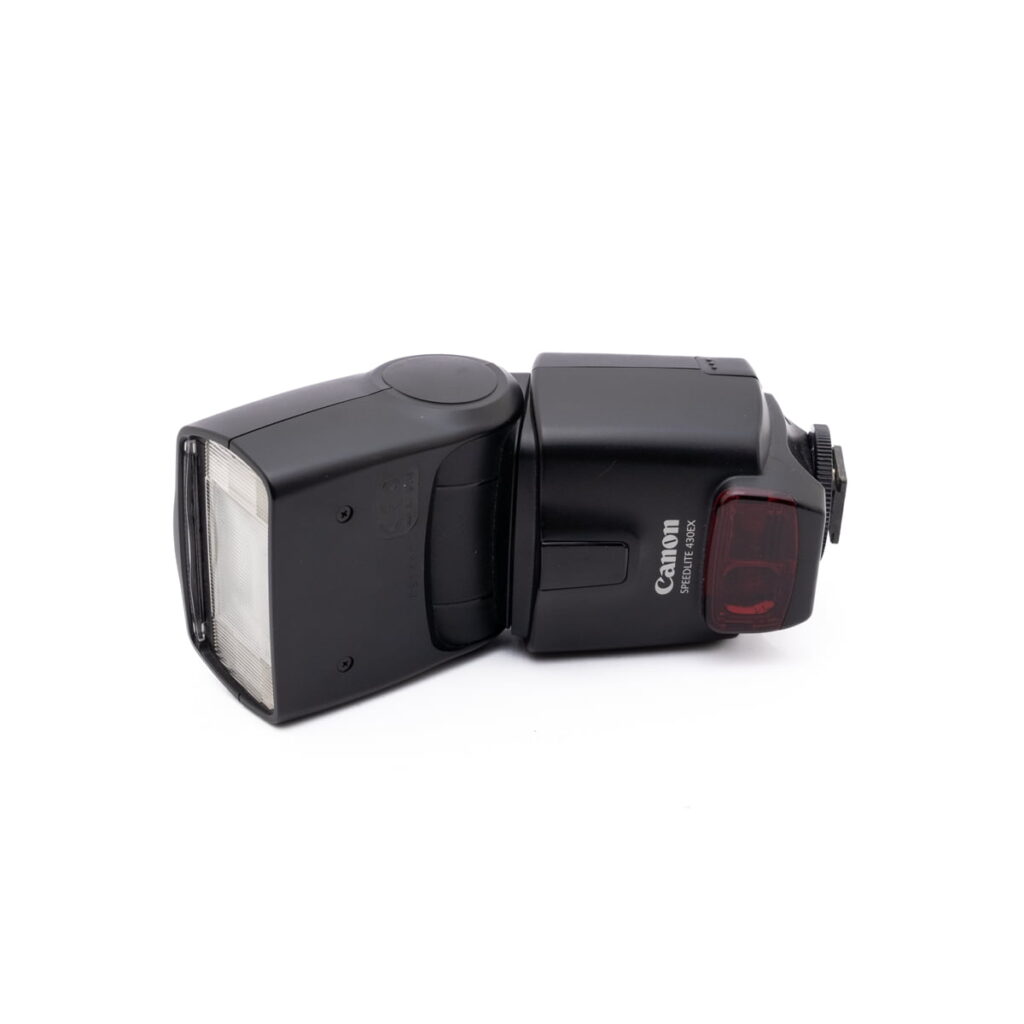 Canon Speedelite 430ex-1 Musta Canon Speedlite 430EX - Käytetty -kamerasalama lepää valkoisella pohjalla vasemmalle kallistettuna, ja sen rungossa näkyy Canon-logo ja mallinimi.