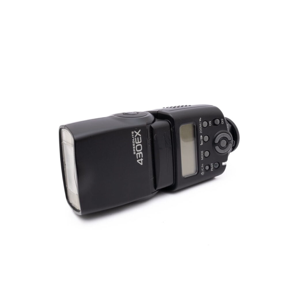 Canon Speedelite 430ex-2 Mustaa Canon Speedlite 430EX - Käytetty ulkoinen kamerasalama on suunnattu valkoiselle taustalle, ja sen LCD-näyttö ja ohjauspainikkeet ovat näkyvissä.