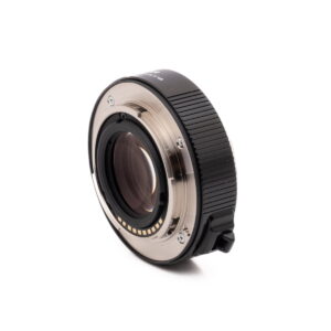 Fujinon 1.4x converter-3 Olympus OM-D E-M1X (SC 460) - Käytetty kameran objektiivisovitin, jossa on metallinen kiinnitys, elektroniset koskettimet, musta uurrettu pinta ja lukitusvipu, valkoista taustaa vasten.