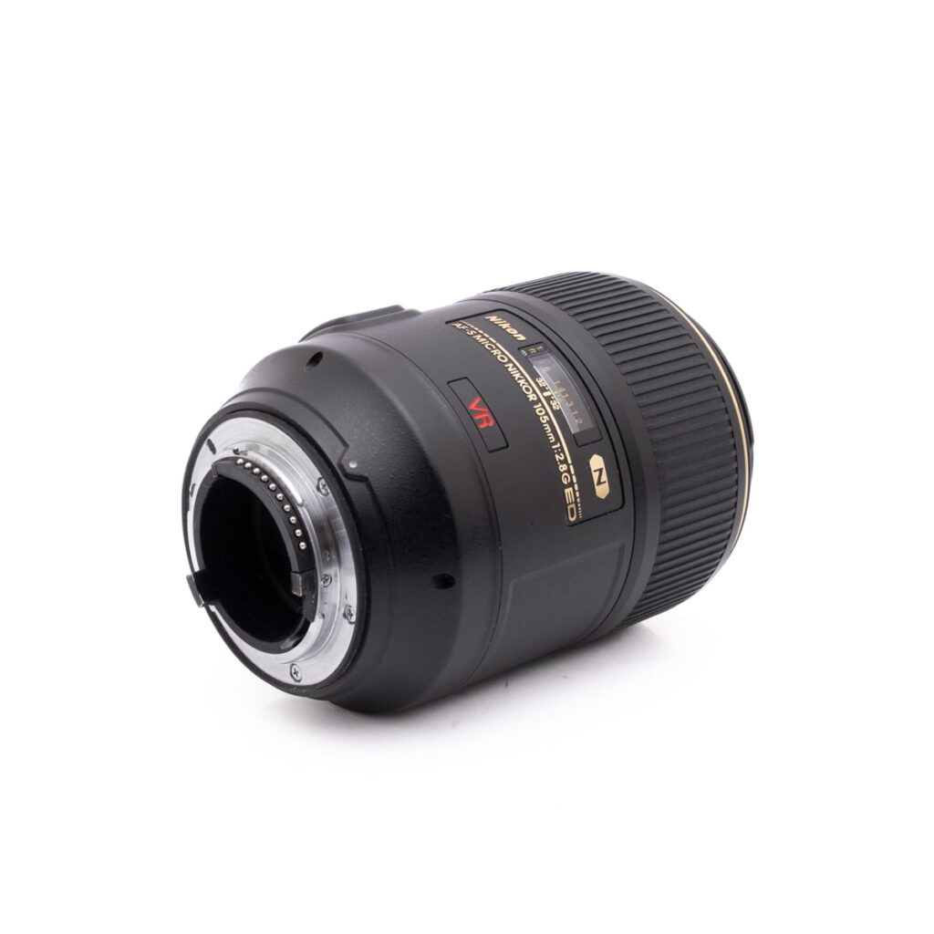 Nikon Nikkor Z DX 16-50mm f/3.5-6.3 VR - Käytetty -objektiivin lähikuvassa näkyy objektiivin musta muotoilu kultaisilla korostuksilla. Objektiivi makaa kyljellään ja siinä on näkyvissä objektiivin kiinnitys ja elektroniset kontaktit valkoista taustaa vasten.