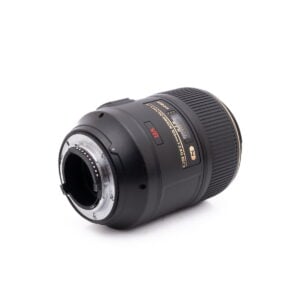 Nikon Nikkor Z DX 16-50mm f/3.5-6.3 VR - Käytetty -objektiivin lähikuvassa näkyy objektiivin musta muotoilu kultaisilla korostuksilla. Objektiivi makaa kyljellään ja siinä on näkyvissä objektiivin kiinnitys ja elektroniset kontaktit valkoista taustaa vasten.