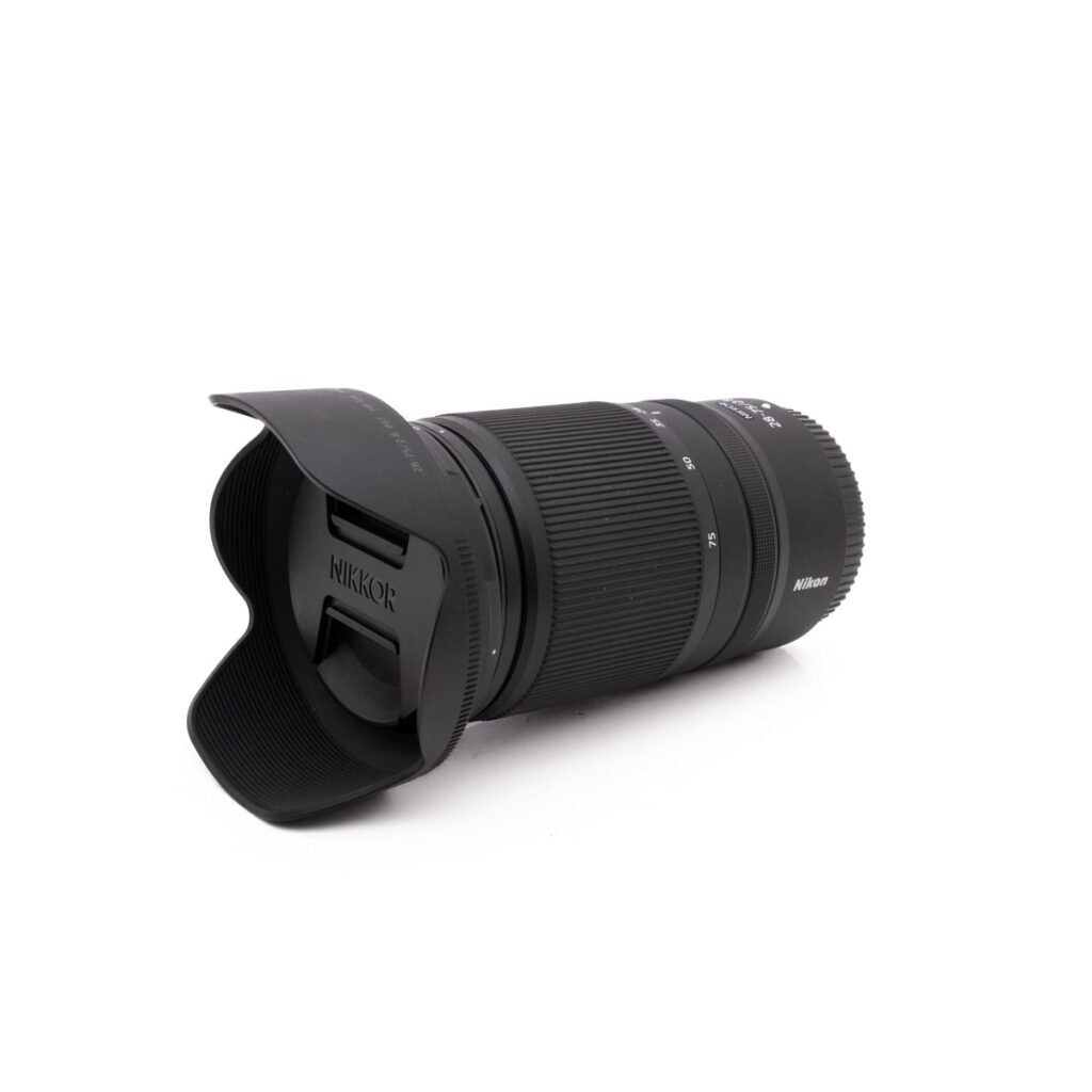 Nikkor 28-75mm f2.8-1 Sigma 30mm f/1.4 DC DN Sony E - Käytetty objektiivi, johon on kiinnitetty vastavalosuoja, lepää valkoisella pinnalla kulmassa, joka korostaa tuotemerkkiä ja kuvioitua kahvaa.