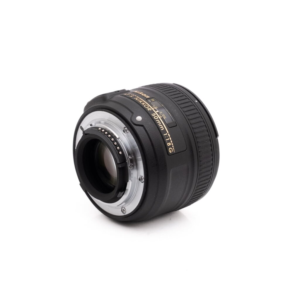 Nikon Nikkor Z DX 16-50mm f/3.5-6.3 VR - Käytetty on musta DSLR-objektiivi, jossa on kullanvärinen ja valkoinen teksti, kuvattuna kulmikkaasta takakuvasta valkoisella taustalla, jossa näkyy objektiivin kiinnitys ja elektroniset kontaktit.