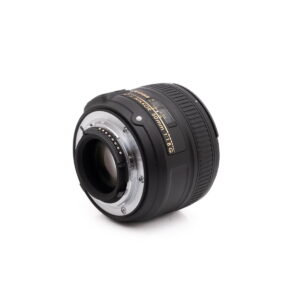Nikon Nikkor Z DX 16-50mm f/3.5-6.3 VR - Käytetty on musta DSLR-objektiivi, jossa on kullanvärinen ja valkoinen teksti, kuvattuna kulmikkaasta takakuvasta valkoisella taustalla, jossa näkyy objektiivin kiinnitys ja elektroniset kontaktit.
