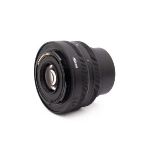 Nikkor Z 16-50mm f3.5-6.3-3 Nikon Nikkor Z DX 16-50mm f/3.5-6.3 VR - Käytetty musta kameraobjektiivi näkyy valkoisella pohjalla vinossa kulmassa, jossa näkyy sekä etulasielementti että elektroniset koskettimet sen metallisessa kiinnityksessä.