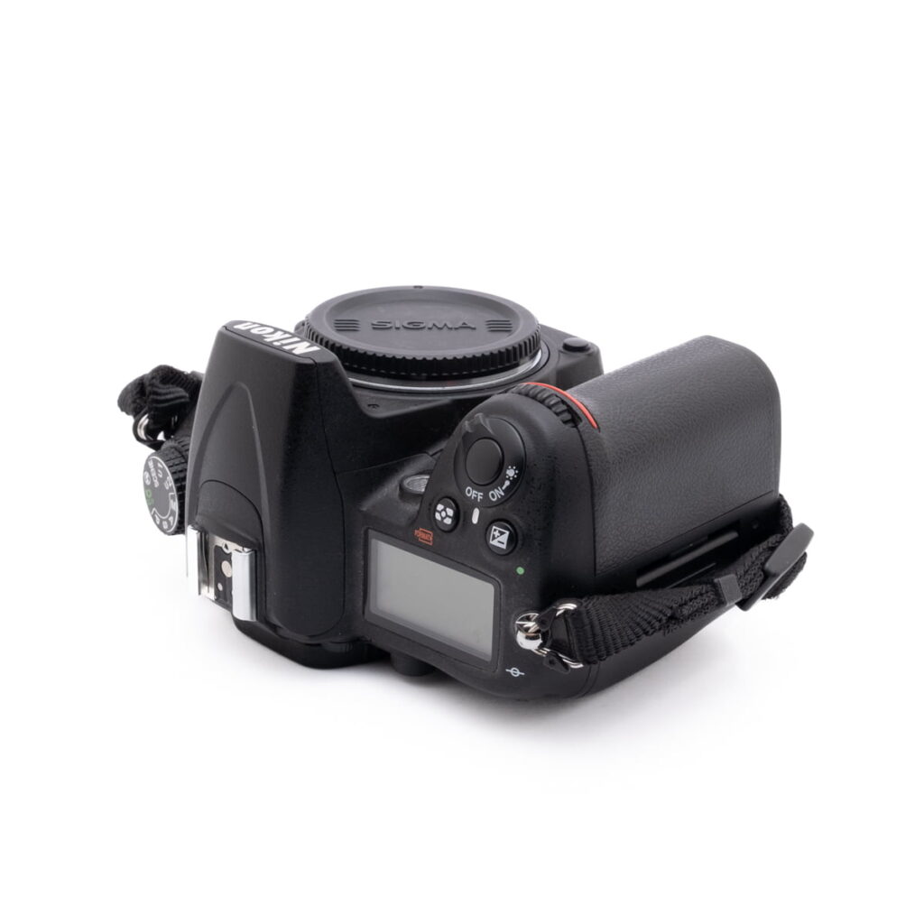 Nikon D7000-4 Nikon D7000 (SC 7000) - Käytetty digitaalikameran runko, jossa on Sigma-objektiivin suojus, näyttö, ohjauspainikkeet ja musta hihna valkoisella pohjalla.
