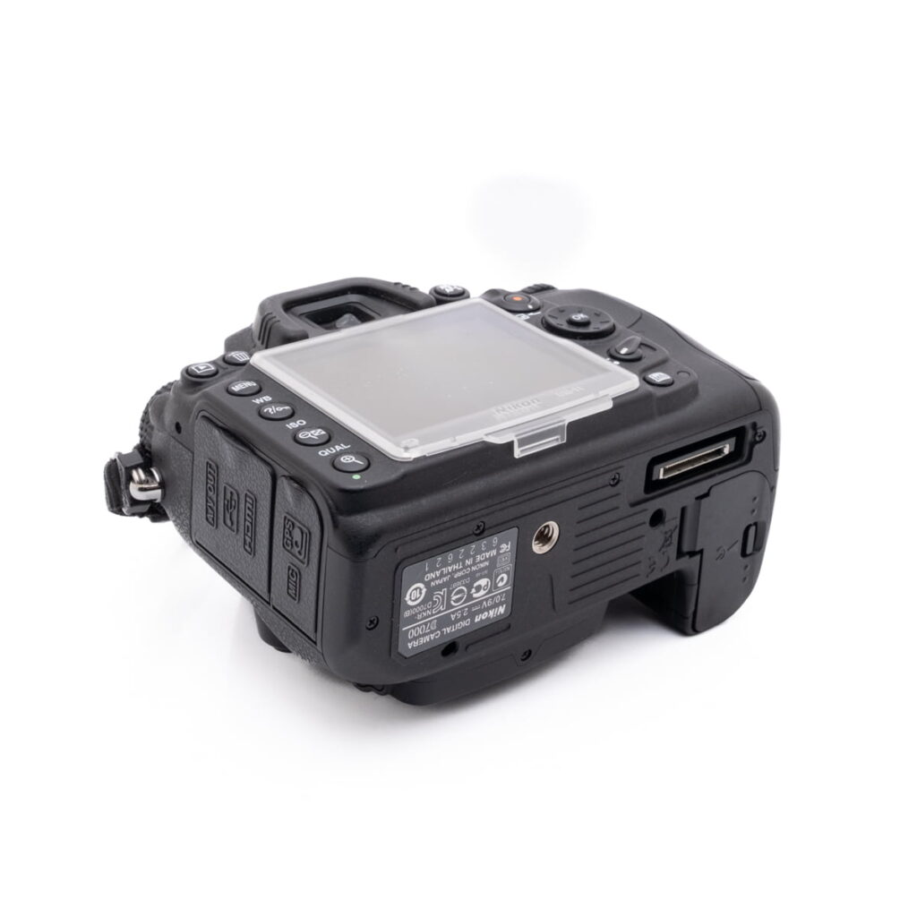 Nikon D7000-5 Nikon D7000 (SC 7000) - Käytetty DSLR-kamera mustana, takaa oikeasta kulmasta katsottuna, selkeä LCD-näytön suojus, useita ohjauspainikkeita, portteja ja muistikorttipaikka näkyvissä.
