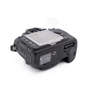 Nikon D7000-5 Nikon D7000 (SC 7000) - Käytetty DSLR-kamera mustana, takaa oikeasta kulmasta katsottuna, selkeä LCD-näytön suojus, useita ohjauspainikkeita, portteja ja muistikorttipaikka näkyvissä.