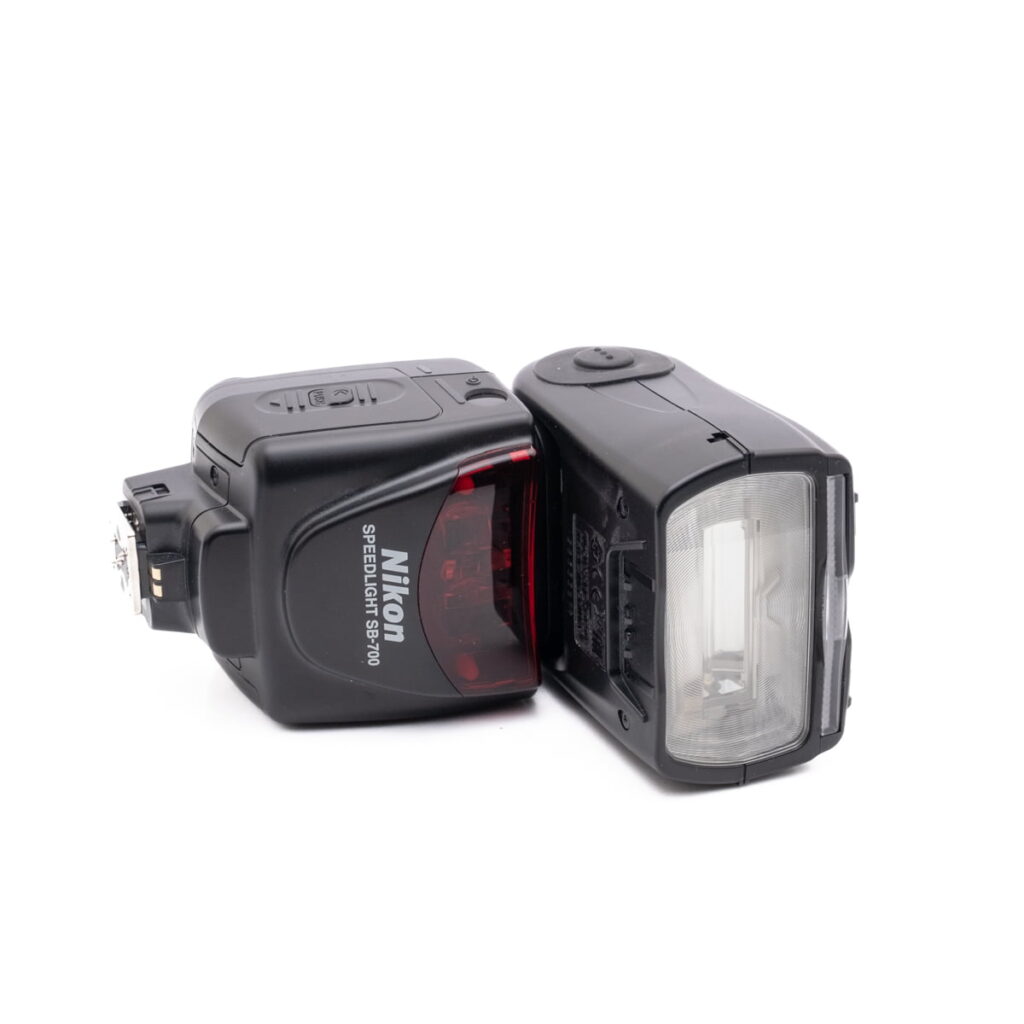 Nikon speedlight SB-700-3 Nikon AF-S Nikkor 50mm f/1.8 G (Kunto K4.5) - Käytetty -objektiivi on kuvattu valkoisella pohjalla kyljellään siten, että objektiivin elementit ja tarkennusrengas ovat näkyvissä.