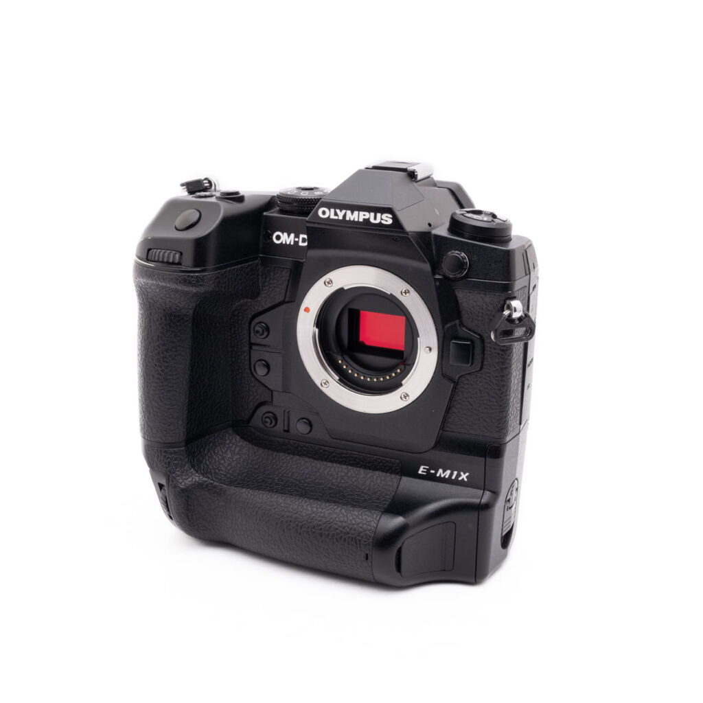 Olympus OM-D E-M1X-2 Musta Olympus OM-D E-M1X (SC 460) - Käytetty kamerarunko ilman objektiivia, jossa on kuvakenno ja näkyvä käsikahva, on asetettu valkoista taustaa vasten.