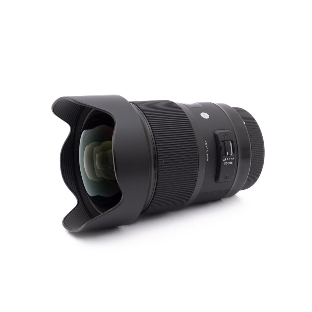 Sigma 20mm f1.4 Canon-1 Olympus OM-D E-M1X (SC 460) - Käytetty -kamerassa on musta runko, kuvioitu kahva ja automaattitarkennuksen/manuaalitarkennuksen kytkimet, jotka on esitetty valkoisella pinnalla.