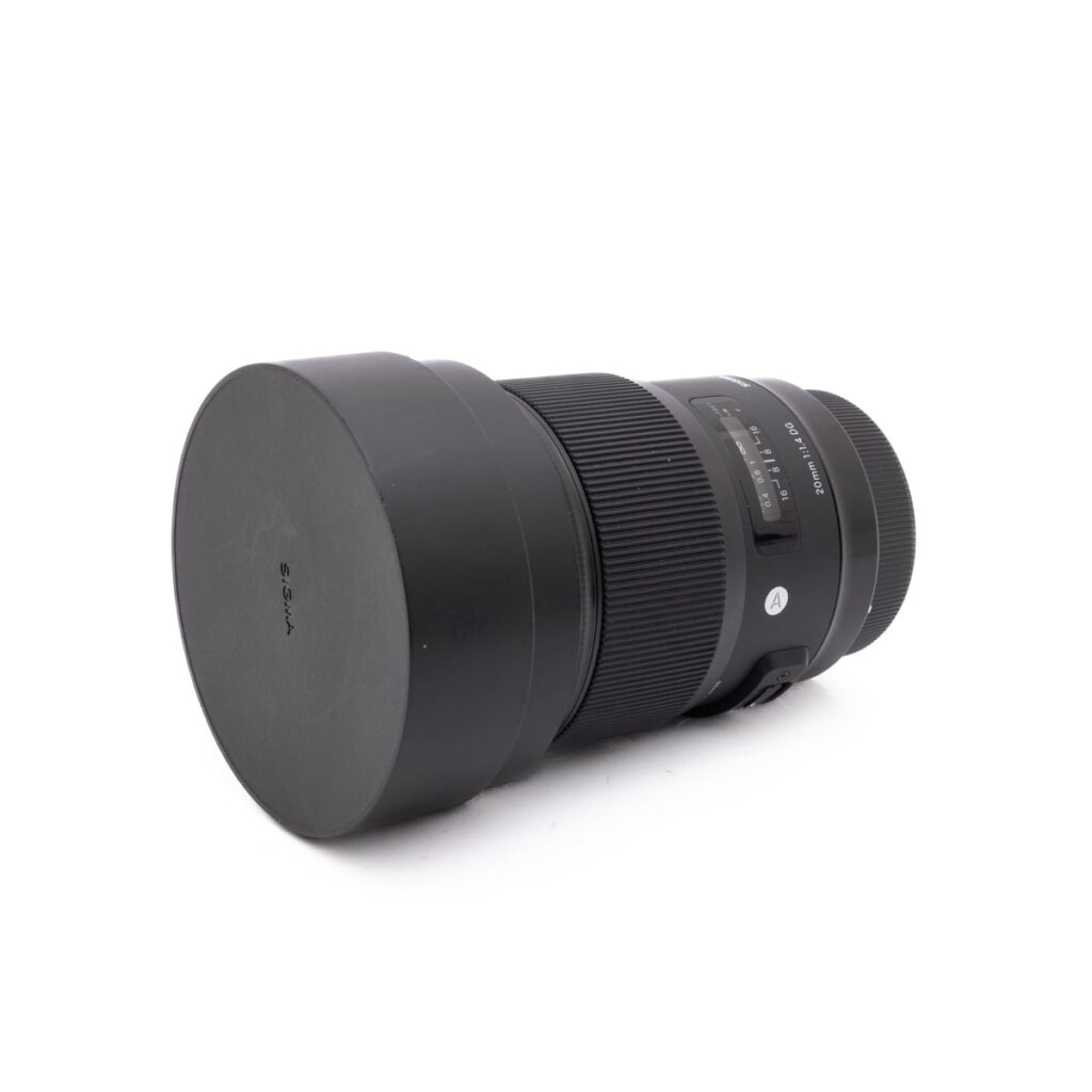 Sigma 20mm f1.4 Canon-2 Olympus OM-D E-M1X (SC 460) - Käytetty kamera on esitetty vaakasuorassa mustalla objektiivilla ja vastavalosuojalla valkoisella pohjalla.