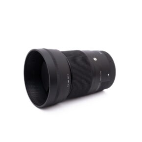 Sigma 30mm f1.4 SonyE-1 Sigma 30mm f/1.4 DC DN Sony E - Käytetty musta kameraobjektiivi, jossa on uurrettu tarkennusrengas ja vastavalosuoja, on kuvattu valkoisella taustalla hieman vasemmalle suunnattuna.