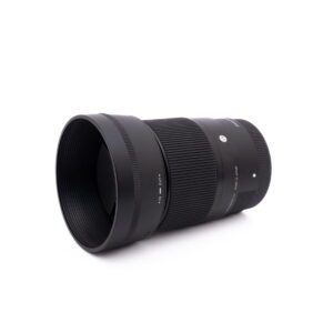 Sigma 30mm f1.4 SonyE-1 Sigma 30mm f/1.4 DC DN Sony E - Käytetty musta kameraobjektiivi, jossa on uurrettu tarkennusrengas ja vastavalosuoja, on kuvattu valkoisella taustalla hieman vasemmalle suunnattuna.